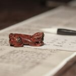 漢文の書かれた紙と筆、赤い文鎮が置かれた書き物机