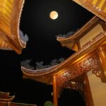 夜の寺院の反り屋根越しに浮かぶ満月