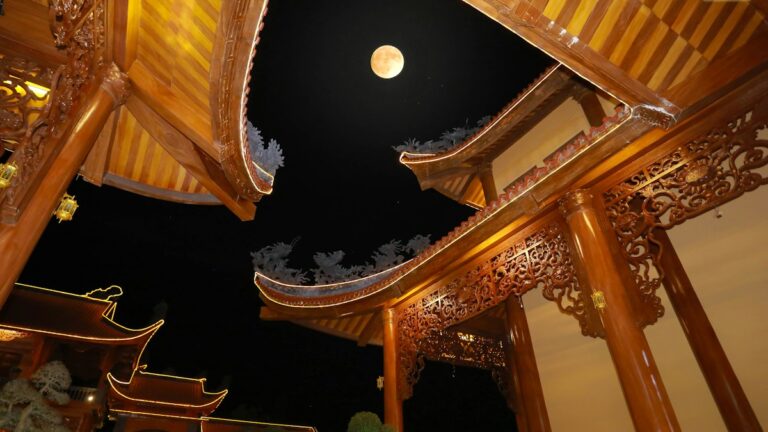 夜の寺院の反り屋根越しに浮かぶ満月