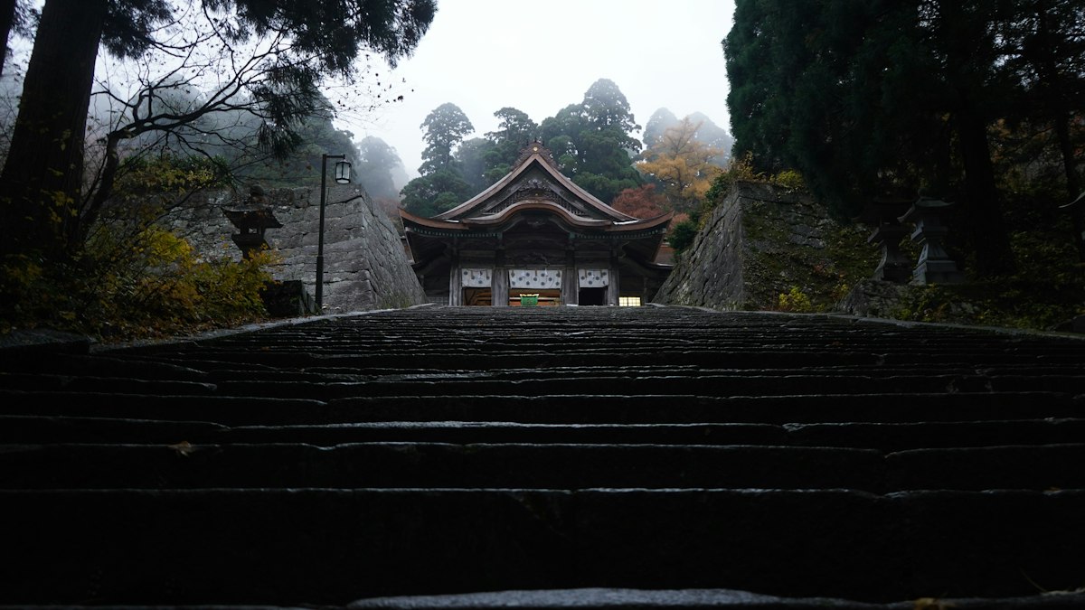 霧に包まれた山中の古い寺へ続く石段