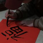 赤い紙に筆で漢字を書く手元