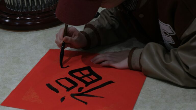 赤い紙に筆で漢字を書く手元