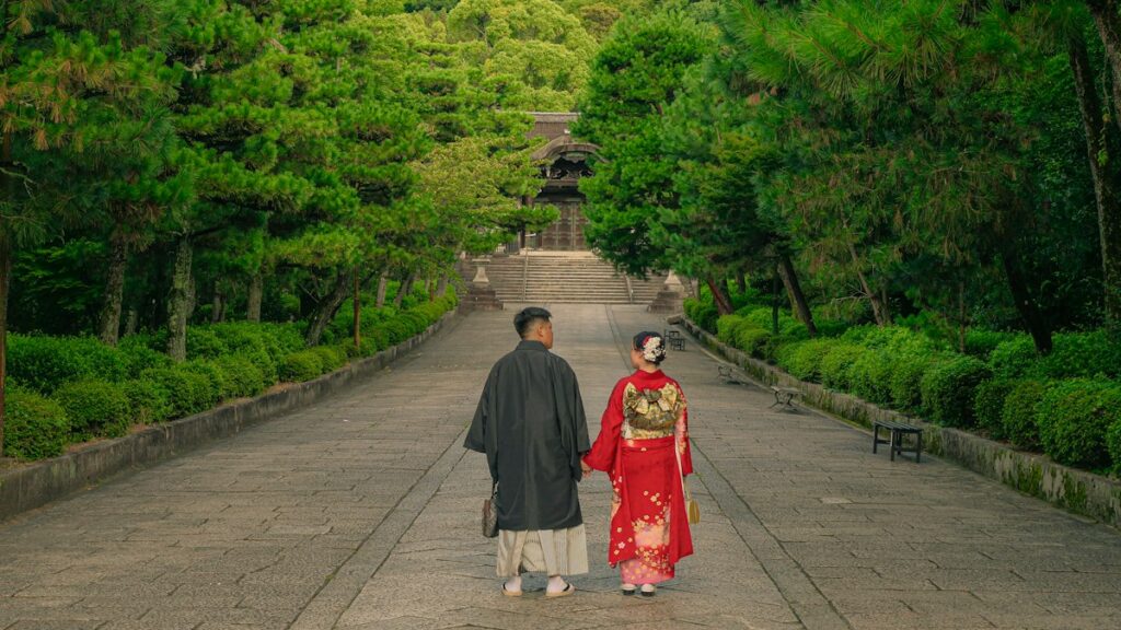 木立に囲まれた寺の参道を並んで歩く和装の二人