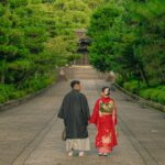 木立に囲まれた寺の参道を並んで歩く和装の二人
