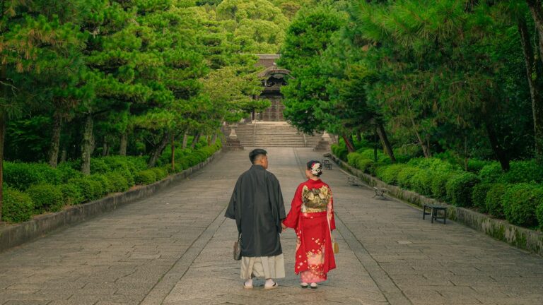 木立に囲まれた寺の参道を並んで歩く和装の二人