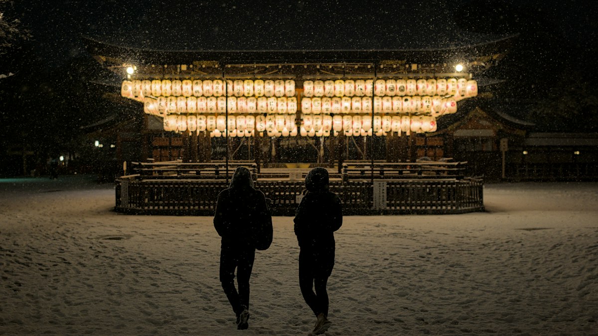 雪の夜に灯りのともる方へ並んで歩く二人の後ろ姿