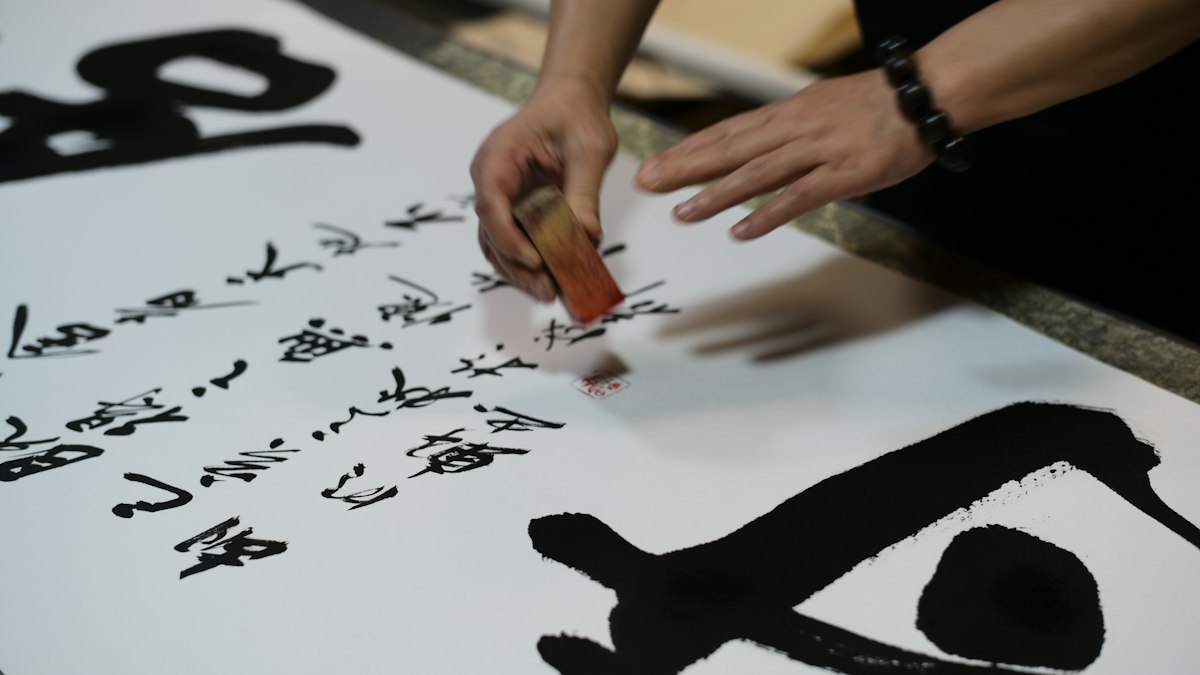 大きな紙に書かれた漢字の書と筆を持つ手