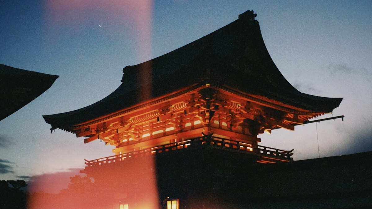 夕暮れの空の下で灯りに照らされる寺の楼門
