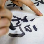 墨で書かれた漢字を指でなぞる手元
