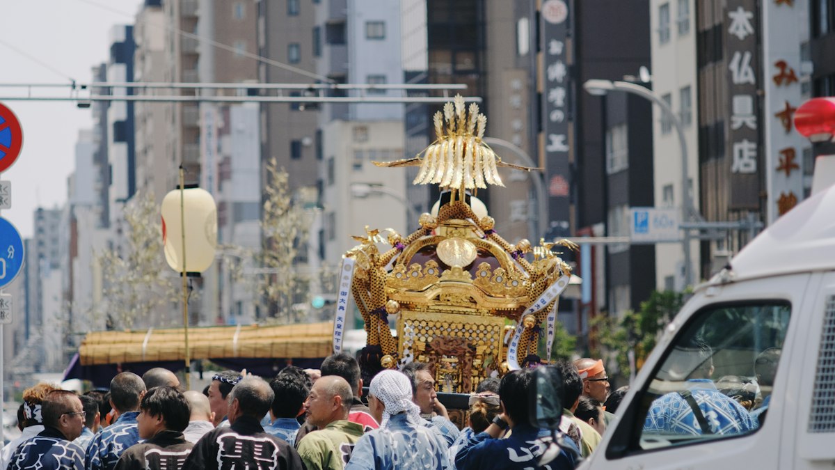 街なかを担がれて進む金色の神輿と祭りの人々