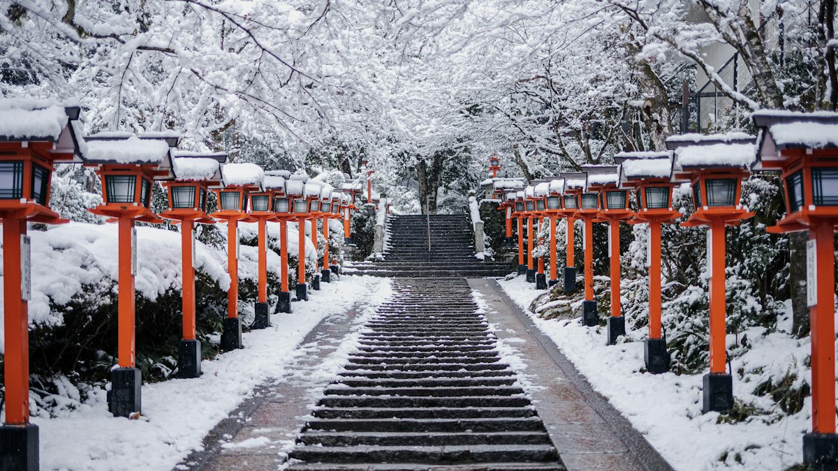 雪の参道に並ぶ朱色の灯籠と石段