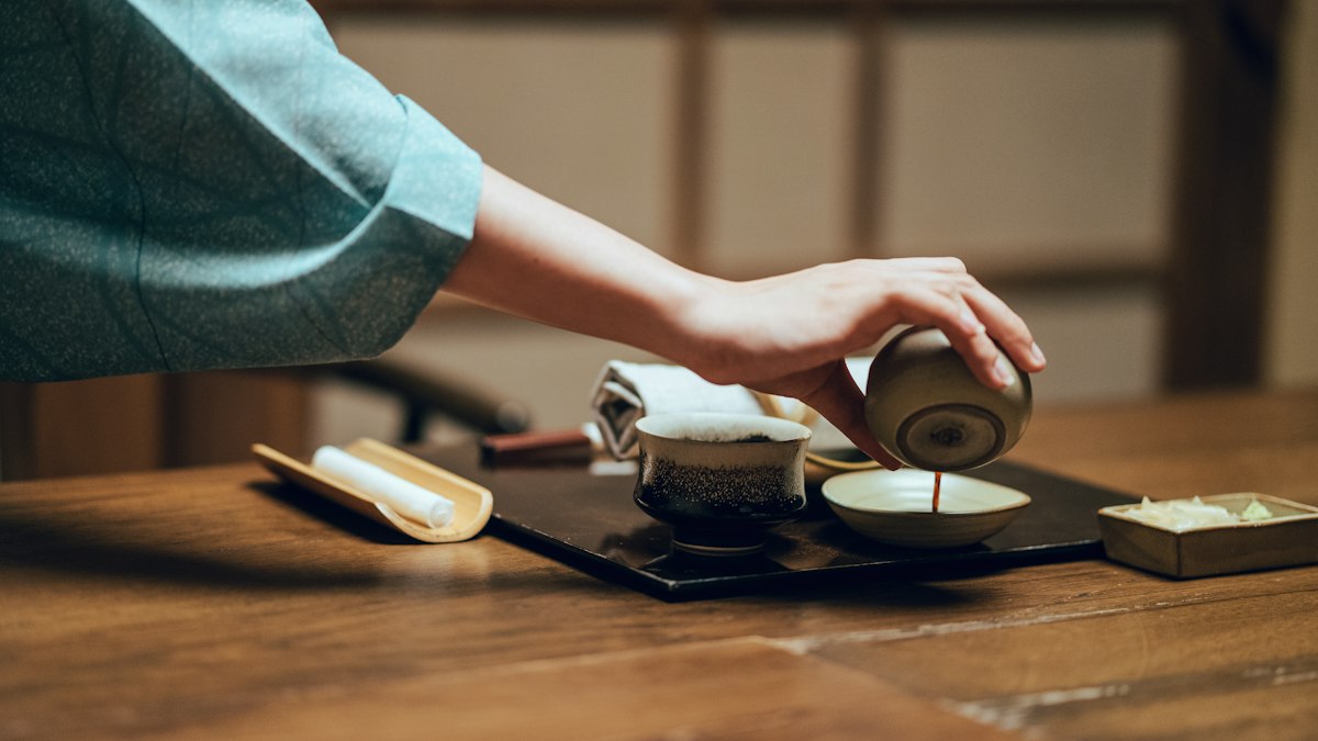 木の卓で茶器に茶を注ぐ手元