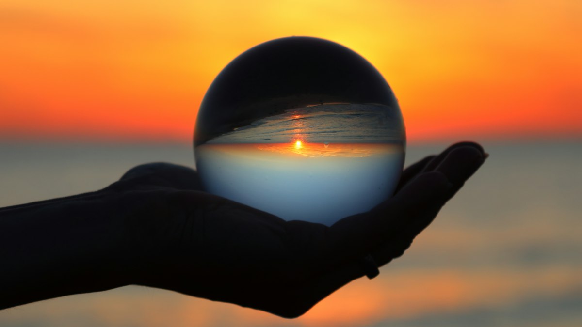 手のひらの水晶玉に逆さに映る夕日の海