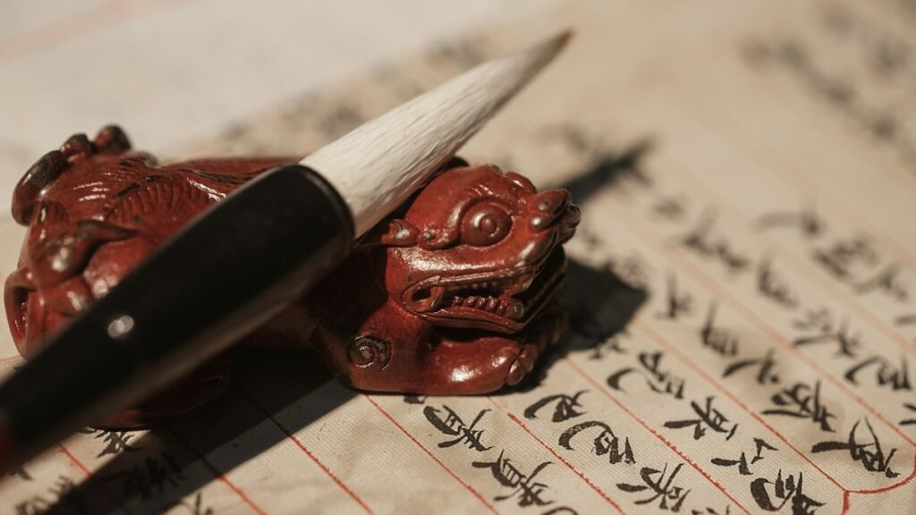 漢字が縦に並ぶ書の上に置かれた筆と朱色の獅子の筆置き
