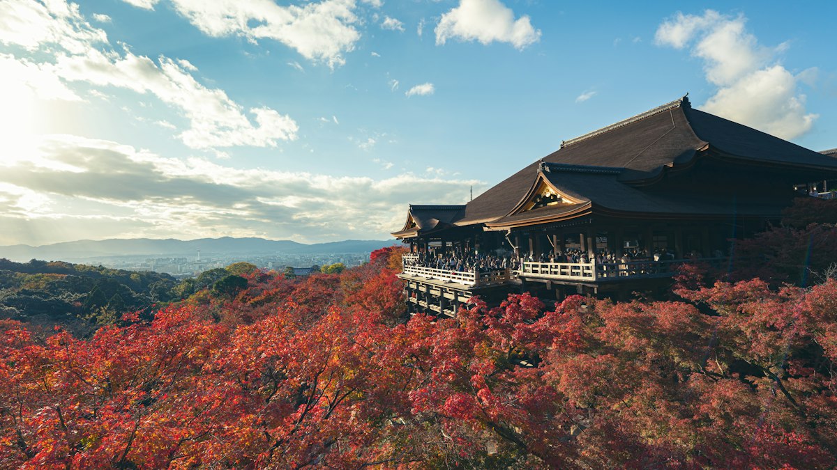 紅葉に包まれた山の上の古い寺の本堂と青空