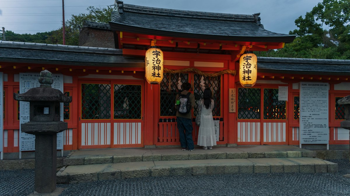 提灯の下がる朱塗りの社殿の前で参拝する人