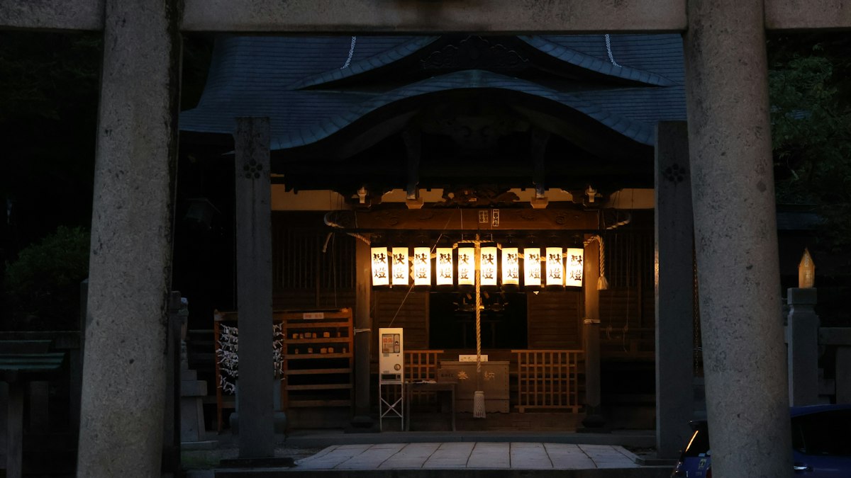 石の鳥居の奥で提灯がともる夕暮れの社殿